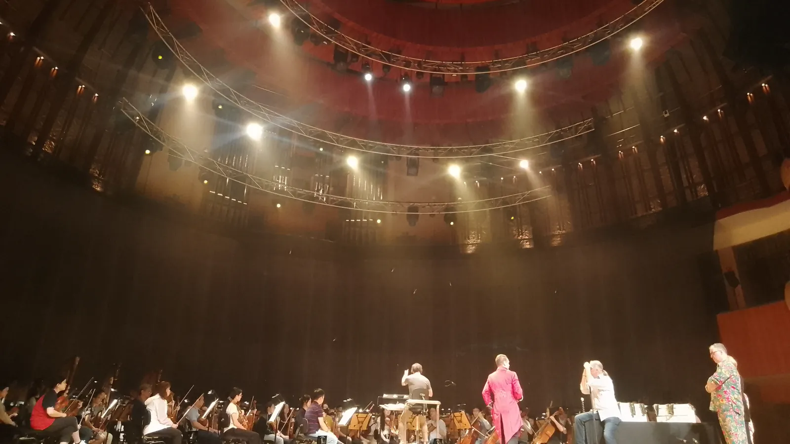 Une troupe de théâtre amateur joue une scène autour d'une grande table, sur un plateau décoré en salle de délibération.
