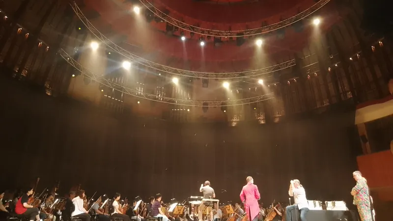 Répétition d'opéra sur la scène d'une grande salle : l'orchestre en fosse et quelques interprètes sous les projecteurs.